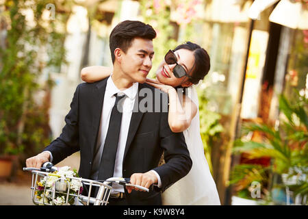 happy newly wed asian couple having fun riding a bicycle. Stock Photo