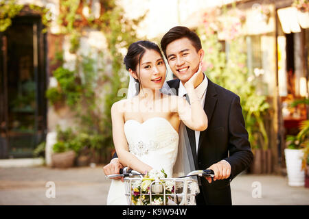 happy newly wed asian couple having fun riding a bicycle. Stock Photo