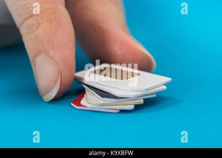 Close-up Of Hand Placing Stack Of Sim Card Over Blue Background Stock Photo