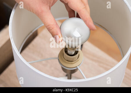 Close-up Of Woman Fixing Lamp On Nightstand Stock Photo