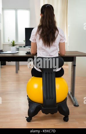 Young Businesswoman Sitting On Fitness Ball While Working On Computer In Office