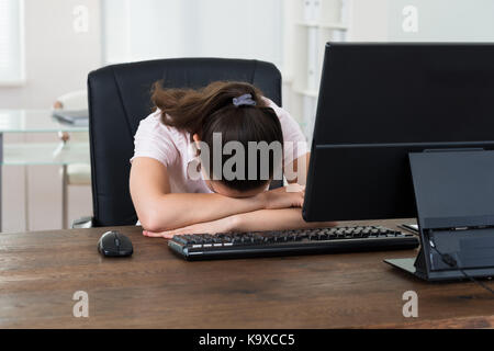 Young Businesswoman Sleeping On Desk In Front Of Computer In Office Stock Photo