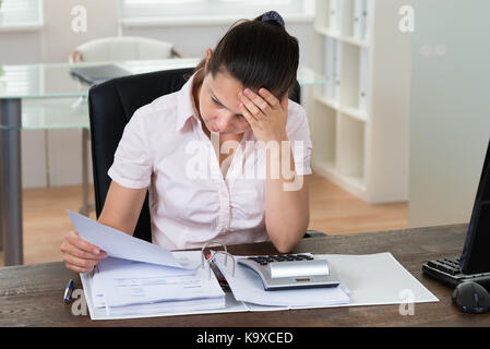 Young Stressed Businesswoman Checking Bills In Office Stock Photo