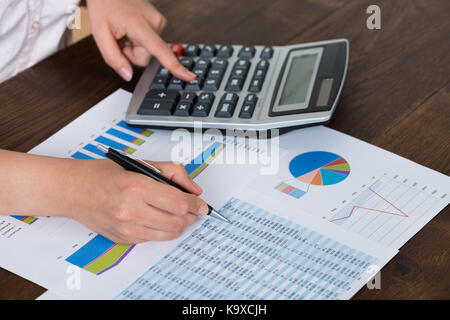 Close-up Of Businesswoman Analyzing Financial Report With Calculator At Wooden Desk Stock Photo