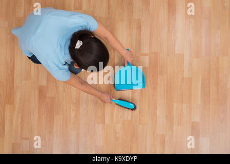 Young Woman Brooming Wooden Floor With Broom And Dustpan Stock Photo