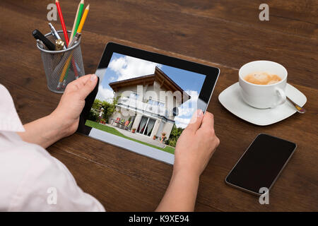 Close-up Of Businessperson Looking At House Photo On Digital Tablet At Desk