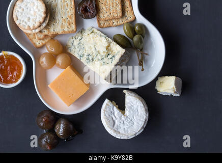 Cheese plate served with various crackers,jam, figs, caper berries and pickled onions. Top view photo with space for text Stock Photo