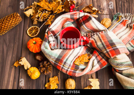 Flatlay of cozy fall setting. Scarf with tea cup and autumn decorations with pumpkins, dried leaves, pine cones on wooden background Stock Photo