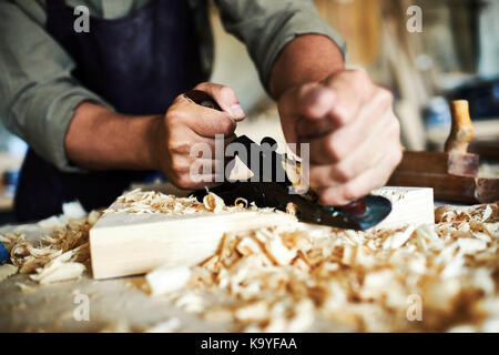 Closeup portrait of strong male hands shaving piece of wood with plane tool in carpenters workshop making furniture Stock Photo