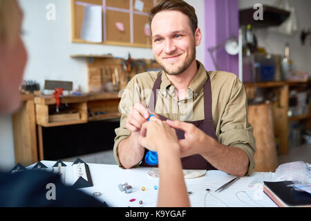 Portrait of smiling young man trying on ring sizes on clients hand in jewelry workshop Stock Photo