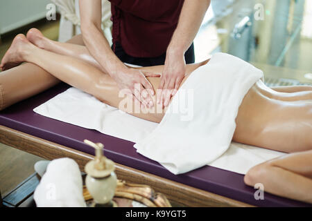 Unrecognizable man massaging legs of young woman lying on massage table in SPA center Stock Photo