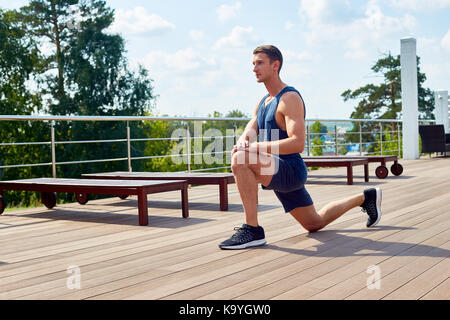 Sporty young man doing forward lunge and enjoying picturesque view while having workout on spacious terrace Stock Photo