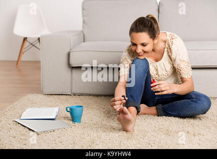 Beautiful happy woman at home making a pause to painting her nails Stock Photo