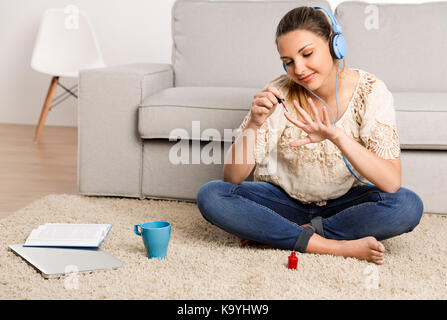 Beautiful woman at home making a pause to painting her nails while listening music Stock Photo