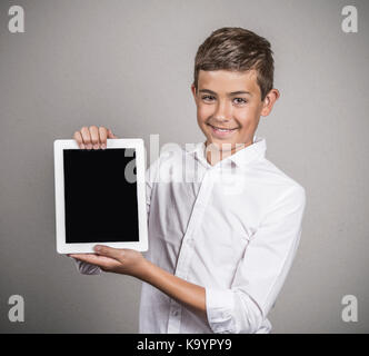 Happy smiling young man, boy holding tablet pad computer present, showing empty touch screen with copy space, isolated grey wall background. Positive  Stock Photo