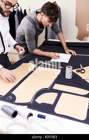 Young tailor making a pattern while her colleague drawing sketches in ...