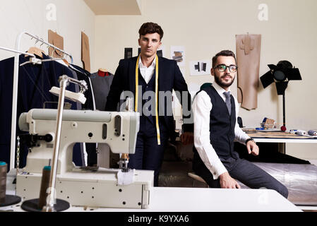 Group portrait of handsome young fashion designers looking at camera while creating promising clothing collection at modern studio Stock Photo