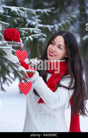 Xmas, winter holidays, Valentine's day and people concept - happy young woman decorating christmas tree. Winter outdoor portrait of girl in sweater, r Stock Photo