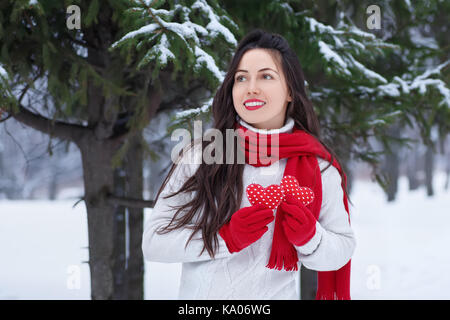 Girl in winter forest holding red hearts in hands. Winter holidays, Valentine's day, people concept. Winter outdoor portrait of young woman in sweater Stock Photo