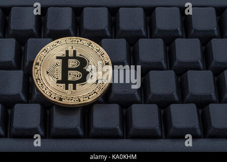 Gold coloured BitCoin / Bitcoin cryptocurrency token on a black Qwerty keyboard - metaphor for online transactions, Darkweb cybercrime, & e-commerce. Stock Photo
