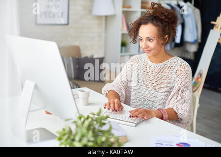 Portrait of smiling young woman working from home at desk with computer in modern apartment Stock Photo