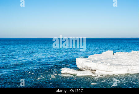 Melting chunks of ice floating out into blue water under empty sky, on Georgian Bay, Ontario, Canada. Stock Photo
