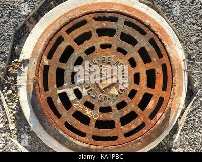 Rusty iron manhole set into asphalt road surfaces Stock Photo