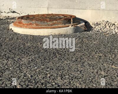 Rusty iron manhole set into asphalt road surfaces Stock Photo