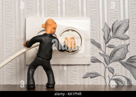 Plasticine man sticks a plug in the socket in the wall of the apartment Stock Photo
