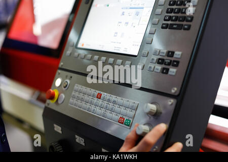The worker controls the operation of the CNC machine using the control panel and the display. Selective focus. Stock Photo
