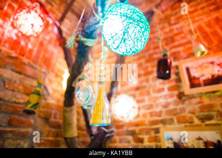 The close-up photo of the small glass bottle hanging on the wooden bricks decorated with handmade colourful balls placed on the cafe brick wall. Stock Photo