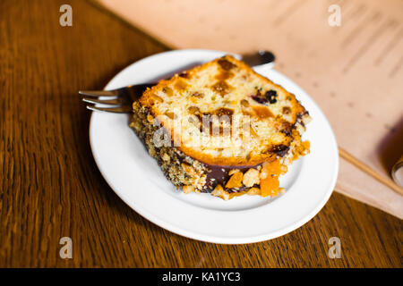 The close-up side view of the piece of the cake covered with chocolate and nuts placed on the wooden table. Stock Photo
