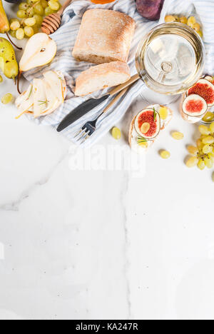 Sandwiches with ricotta or cream cheese, ciabatta, fresh figs, pears, grape, walnuts and honey on white marble table table, with wine glass copy space Stock Photo