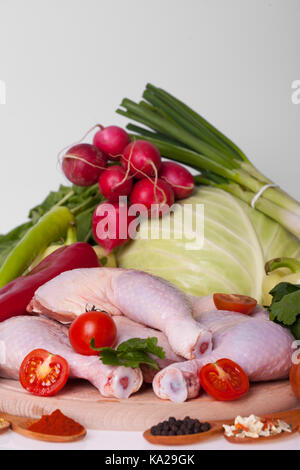 fresh chicken thighs and drumsticks on a wooden board with vegetables. Raw chicken meat with onions, cabbage, radishes and spices in wooden spoons rea Stock Photo