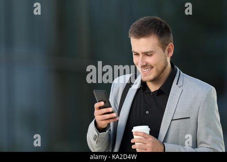One happy executive reading a mobile phone message and holding a take away drink walking on the street Stock Photo