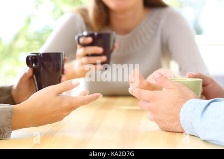 Close up of three friends hands talking and holding coffee cups sitting in a table in a bar or home Stock Photo