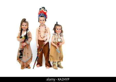 Three little indians, dressed in costumes and holding weapons, greet Thanksgiving with solemn faces.  They stand in all white room with space for pers Stock Photo