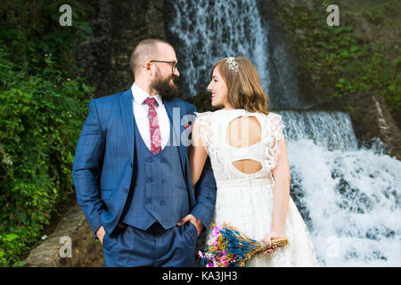 Bride and groom standing in front of a waterfall Stock Photo