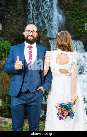 Bride and groom standing in front of a waterfall Stock Photo