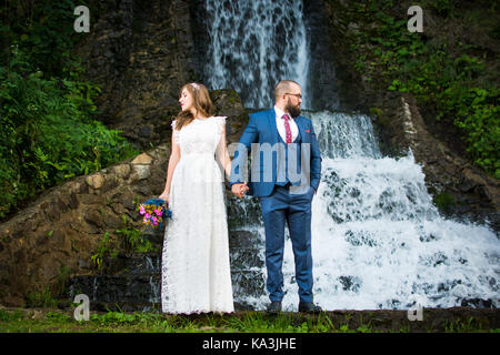 Bride and groom standing in front of a waterfall Stock Photo