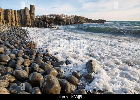 Landscape with rocky seashore and stormy sea and blue sky with clouds. Sun is shining. Waves are breaking on the boulders. Panoramic horizontal photo. Stock Photo