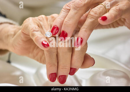 Female manicured hands with diamond. Senior woman hands with red nails and golden ring with diamond. Womans hands with precious jewels. Stock Photo