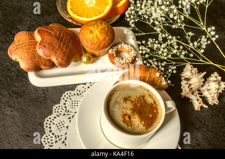 Coffee in white cup and saucer dishes with cakes and chocolate,a saucer with orange slices on black table Stock Photo