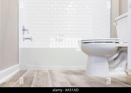 Modern white plain clean toilet bathroom with shower tiles and hardwood floors from ground level Stock Photo