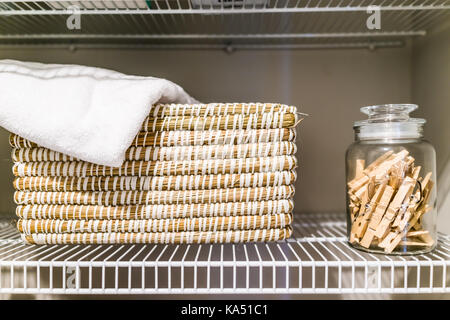 Jar of wooden clothes pegs and woven basket of towels on shelf in closet of laundry room during staging of model house, home or apartment Stock Photo