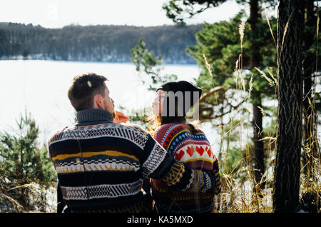 Joyful funny couple in warm clothes in front of frozen lake between forest. Young man hugs the woman. The concept of successful relationship and happy Stock Photo