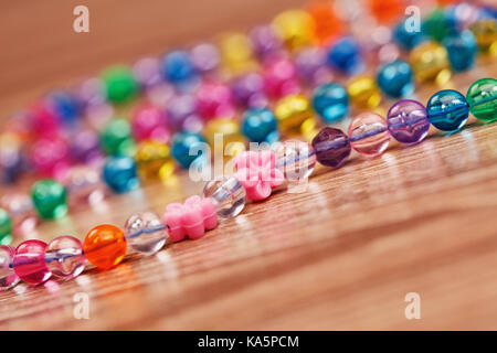 Woven from a colored beads necklace on a wooden table. Stock Photo