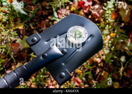 Bitcoin from a silver coin lies or stands on the edge of a small black spade. Search for crypto currencies Stock Photo