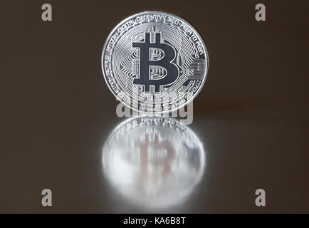 The silver coin bitcoin lies or stands on the edge on a dark mirror background, reflected. The concept of crypto currencies. Stock Photo