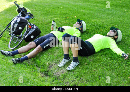 Two touring cyclists cycling on the Hudson Route 9 cycleway resting on green grass after a big hill climb in upstate New York,USA. Stock Photo